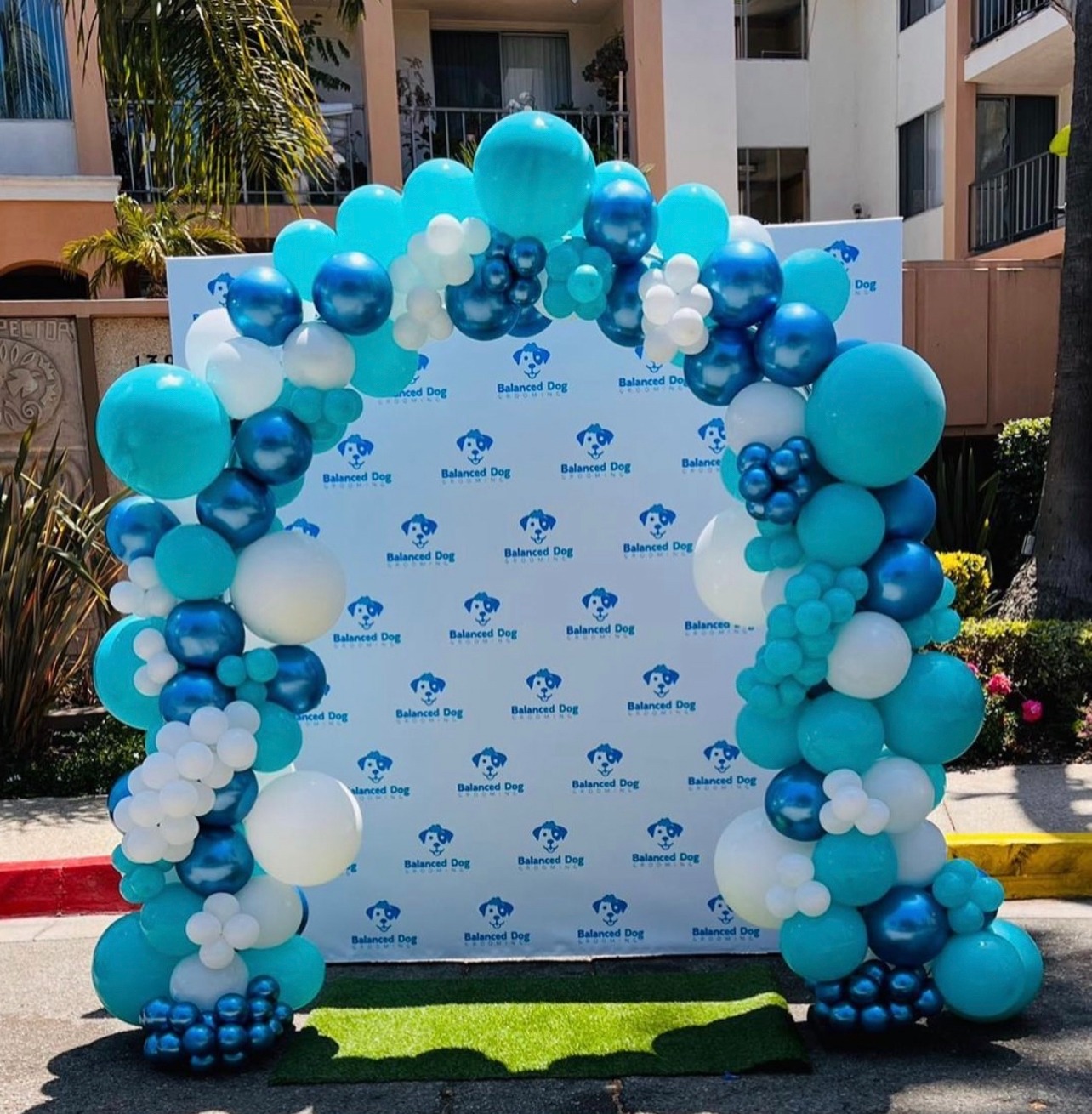 Blue, white and teal organic balloon arch around a branded photo backdrop